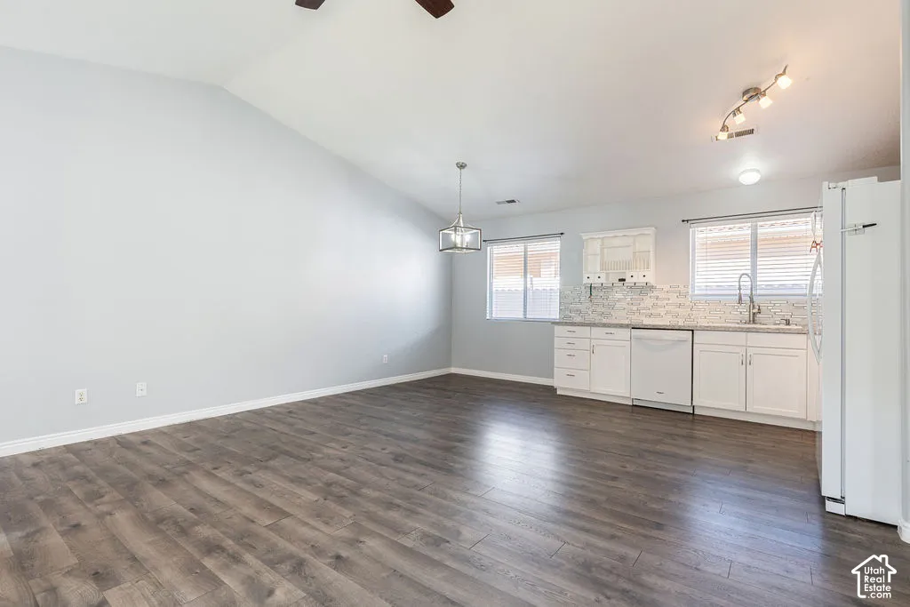 Vaulted ceilings, wood-finish flooring, white shaker-style cabinetry, multi-tone stone backsplash, and adjustable multi-light track fixture