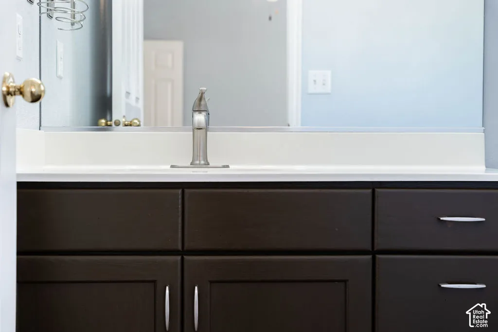 Dark-finish vanity cabinetry with minimalist hardware, white solid-surface countertop, integrated sink, and brushed-nickel single-handle faucet beneath a full-width wall mirror