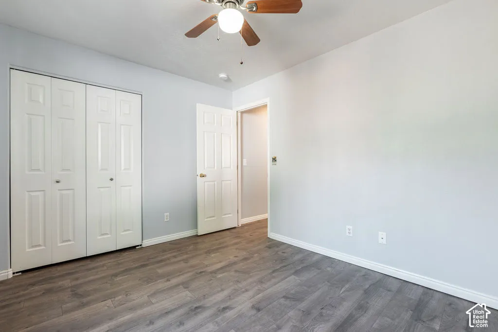 Room featuring wood-finish flooring, a white six-panel swing door, dual-panel closet doors, and a ceiling fan with integrated lighting