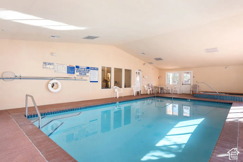 Indoor swimming pool with tile surround, metal handrails, and a built-in spa