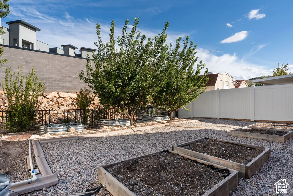 Low-maintenance gravel landscaping featuring multiple raised garden beds, metal planters, mature trees, and perimeter fencing
