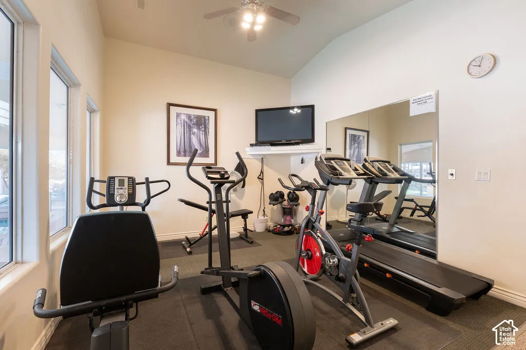 Vaulted ceilings, large windows, wall-mounted television niche, wall-to-wall mirror, and ceiling fan with integrated lighting