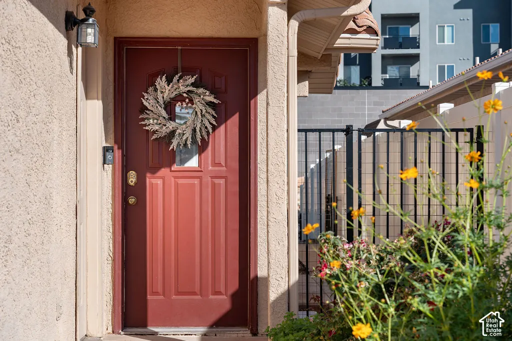 Stucco exterior entryway featuring a solid-panel door with a glass insert, outdoor wall-mounted lighting, and metal perimeter fencing