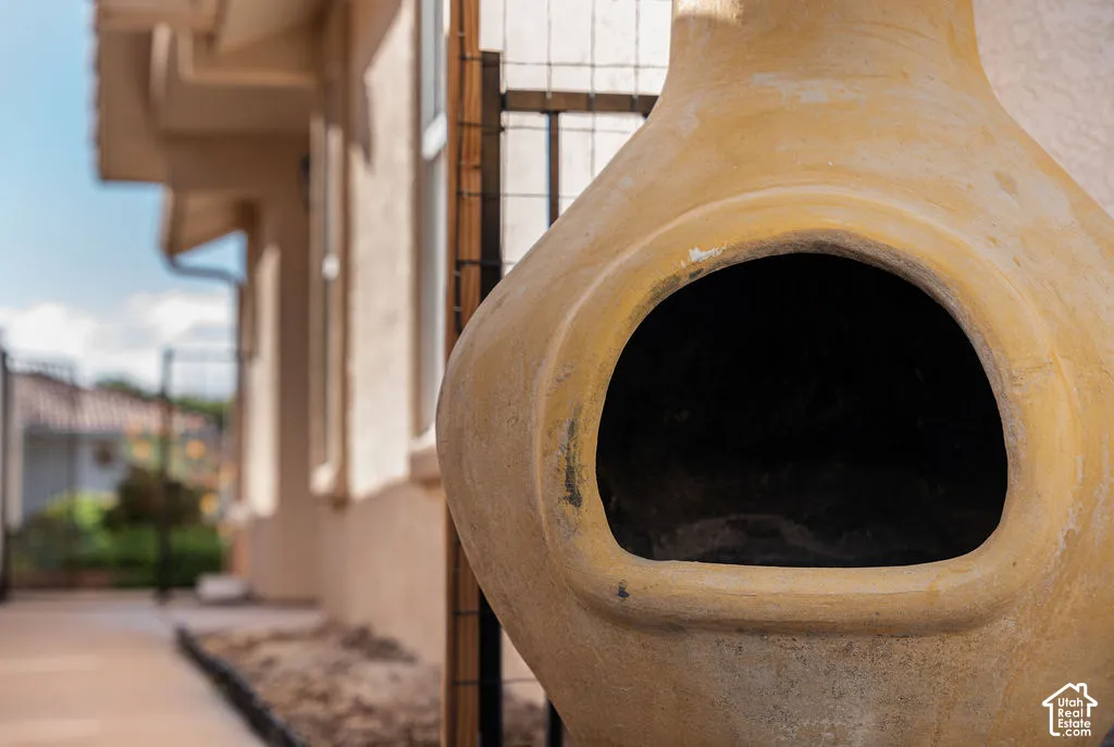 Clay chiminea featuring a textured finish, situated on a paved patio area with exterior stucco wall and wire trellis