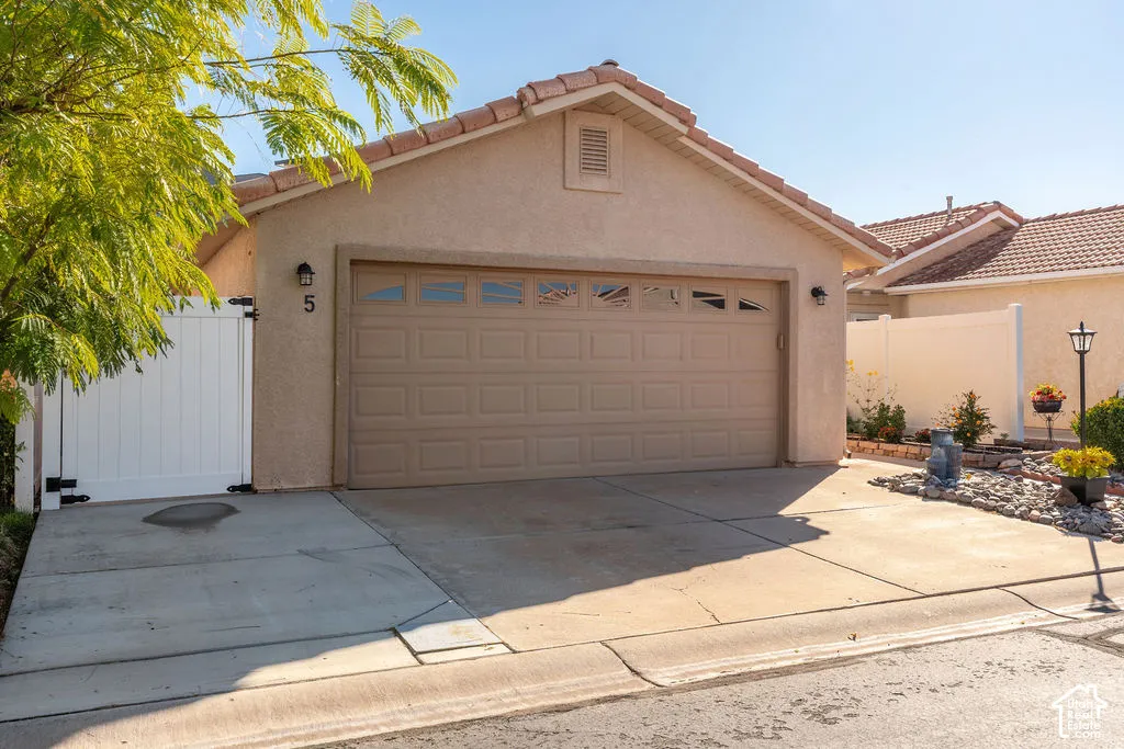Stucco exterior featuring a two-car garage with a sectional door, concrete driveway, tile roof, and white vinyl privacy fencing