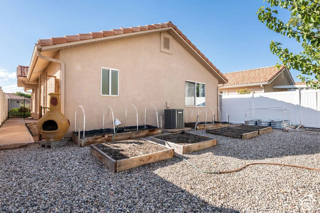 Stucco exterior with a tiled roof, gravel landscaping, multiple raised garden beds, and white vinyl privacy fencing
