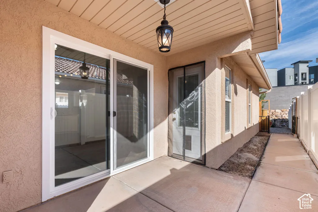 Covered concrete patio featuring sliding glass doors, a decorative pendant light, beige stucco exterior walls, and white vinyl privacy fencing