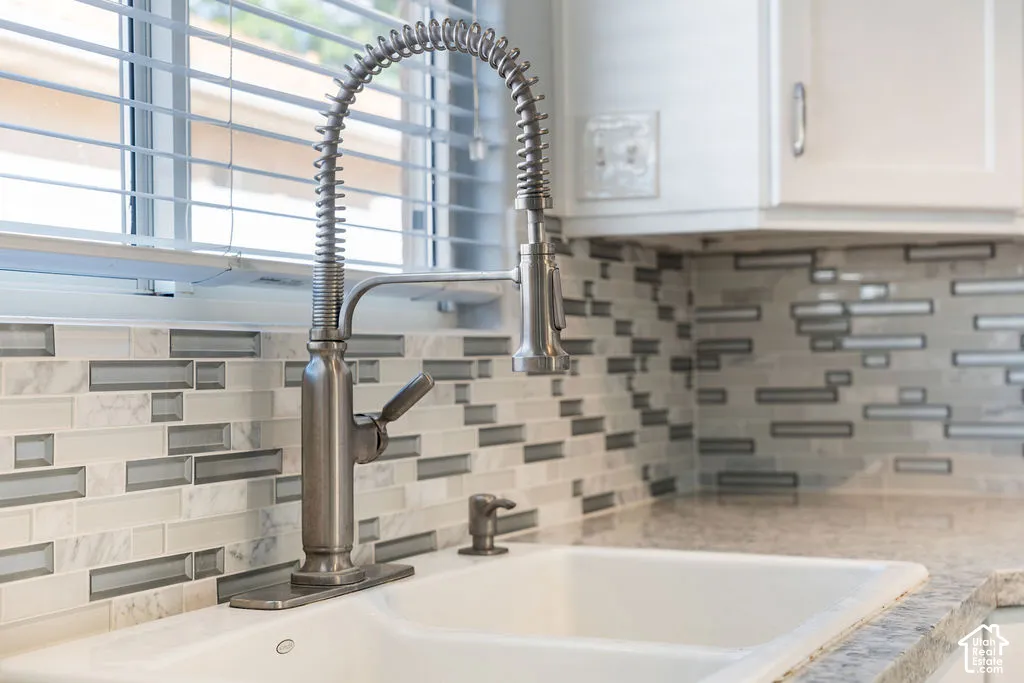 Kitchen sink area featuring a dual-basin undermount sink, a high-arc coiled spring pull-down faucet, stone-patterned countertops, and a multi-textured glass and stone tile backsplash