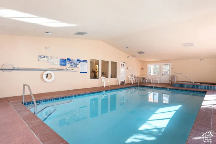 Indoor swimming pool with tile surround, metal handrails, and a built-in spa