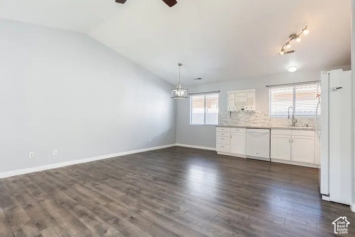 Vaulted ceilings, wood-finish flooring, white shaker-style cabinetry, multi-tone stone backsplash, and adjustable multi-light track fixture