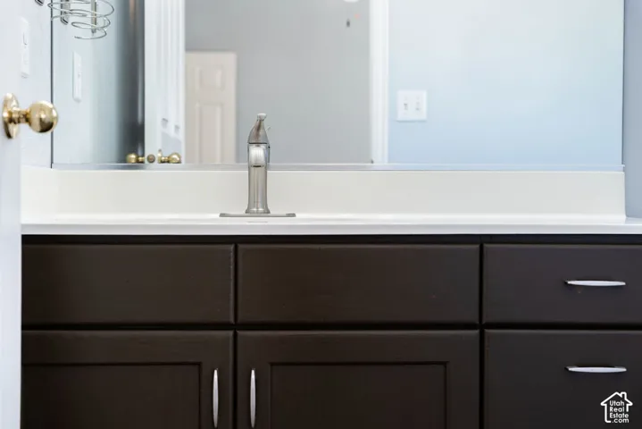 Dark-finish vanity cabinetry with minimalist hardware, white solid-surface countertop, integrated sink, and brushed-nickel single-handle faucet beneath a full-width wall mirror