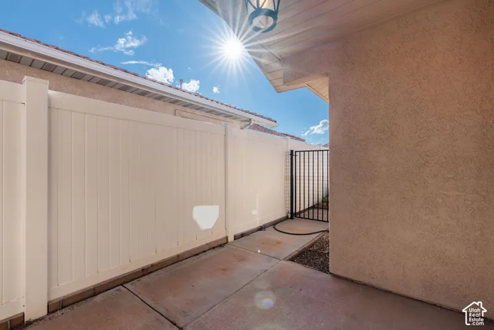 Stucco exterior wall, concrete patio surface, white vinyl privacy fencing, and metal gate