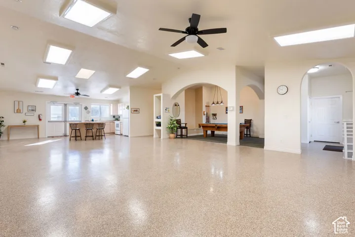 Open-concept interior featuring epoxy-coated flooring, recessed fluorescent lighting, dual ceiling fans, and multiple arched entryways