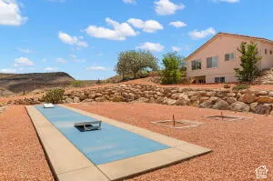 Outdoor recreational area featuring a concrete shuffleboard court, multiple horseshoe pits, tiered natural stone retaining walls, and desert landscaping
