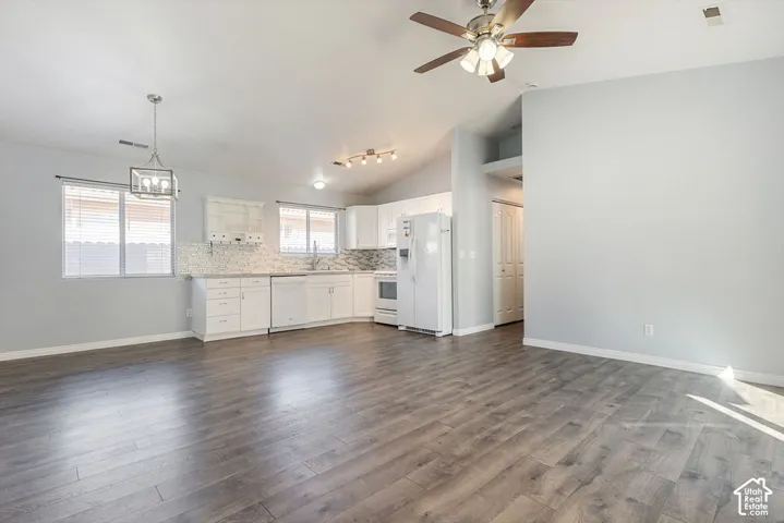 Open-concept interior featuring wood-finish flooring, white cabinetry, a tiled backsplash, and vaulted ceilings with integrated lighting fixtures