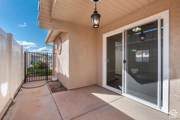 Covered patio featuring concrete flooring, sliding glass door, metal gate, and outdoor pendant lighting