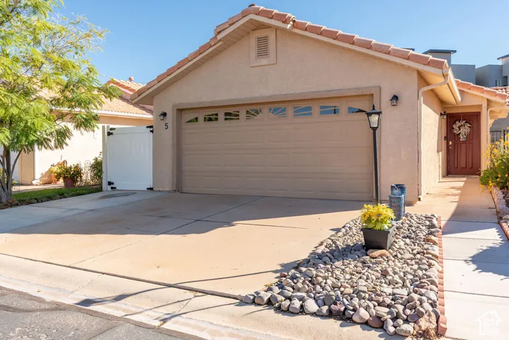 Stucco exterior with a tiled roof, featuring an attached two-car garage with a sectional paneled door and rock-based desert landscaping