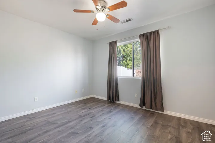Neutral-toned interior room featuring wood-finish flooring, a multi-blade ceiling fan with integrated lighting, and a window with a sliding pane