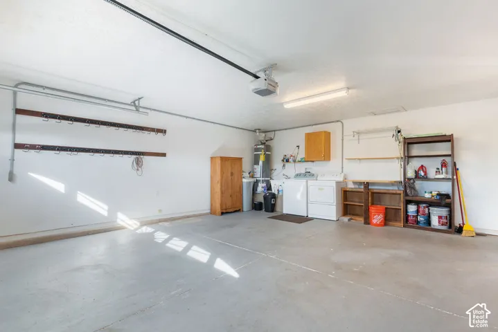 Garage featuring a concrete floor, wall-mounted storage racks, a ceiling-mounted automatic garage door opener, and a dedicated laundry area with utility hookups