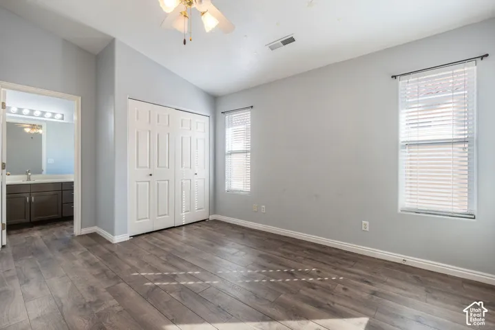 Room featuring wood-finish flooring, vaulted ceilings, dual-panel closet doors, and multi-pane windows with horizontal blinds