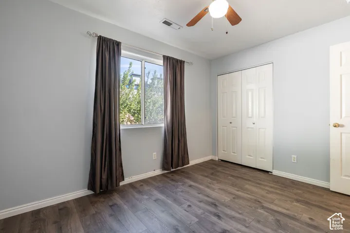Room featuring wood-finish flooring, a ceiling fan with integrated lighting, dual-panel closet doors, and a single-pane window