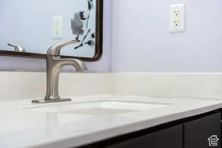 Vanity featuring a white integrated sink and countertop, polished nickel faucet, dark cabinetry, and a framed mirror