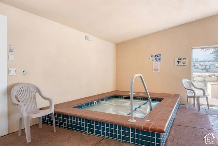 Indoor spa featuring a recessed basin, ceramic tile surround, brick-style coping, and a metal safety handrail