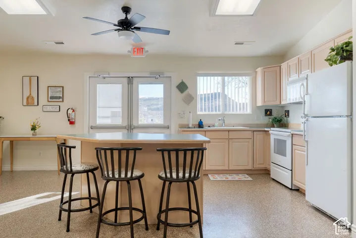 Kitchen featuring light-toned wood cabinetry, a central island with a flat surface, white appliances, recessed ceiling lighting, and double-door exterior access