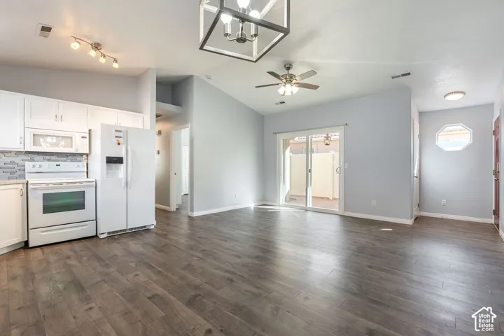 Kitchen featuring white cabinetry, tile backsplash, and built-in appliances, complemented by wood-finish flooring, vaulted ceilings, and a geometric pendant light fixture