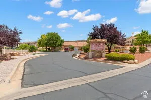 Asphalt driveway featuring stone monument signage, xeriscaping, and mature trees