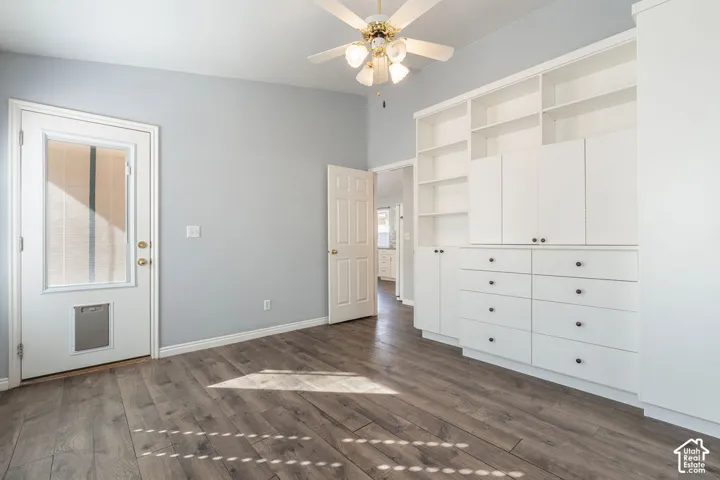 Room featuring wood-finish flooring, vaulted ceiling with a four-light ceiling fan, and extensive built-in white cabinetry with open shelving and drawers