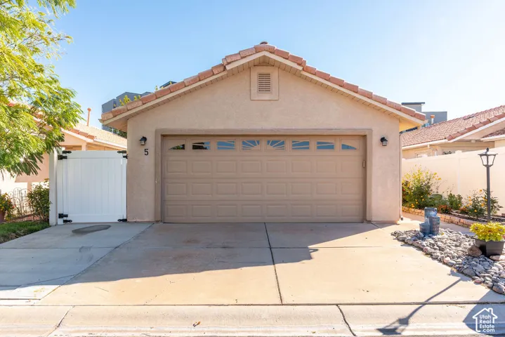 Stucco exterior featuring a two-car garage with transom windows, tile roofing, concrete driveway, and white vinyl privacy fencing