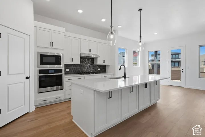 Kitchen featuring white shaker-style cabinetry, an expansive central island with a solid-surface countertop, matte black hardware, integrated stainless steel appliances, and wood-finish flooring