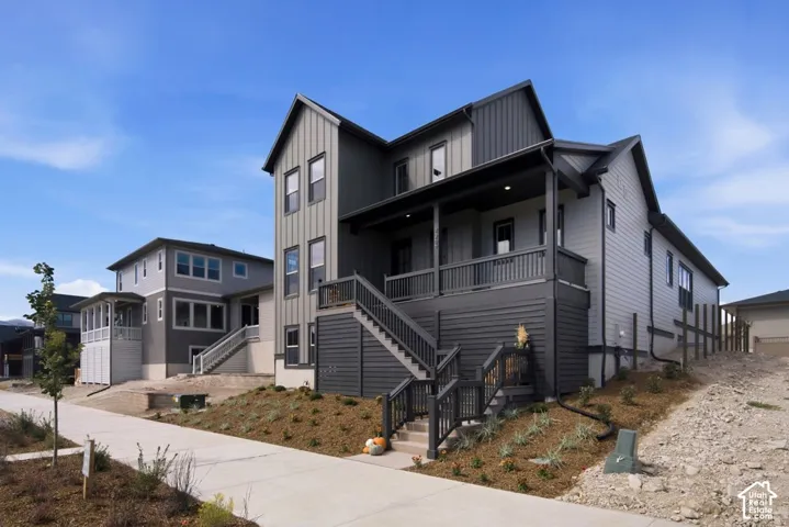 Two-story exterior featuring vertical and horizontal siding, covered porch, dark metal railings, and concrete staircase