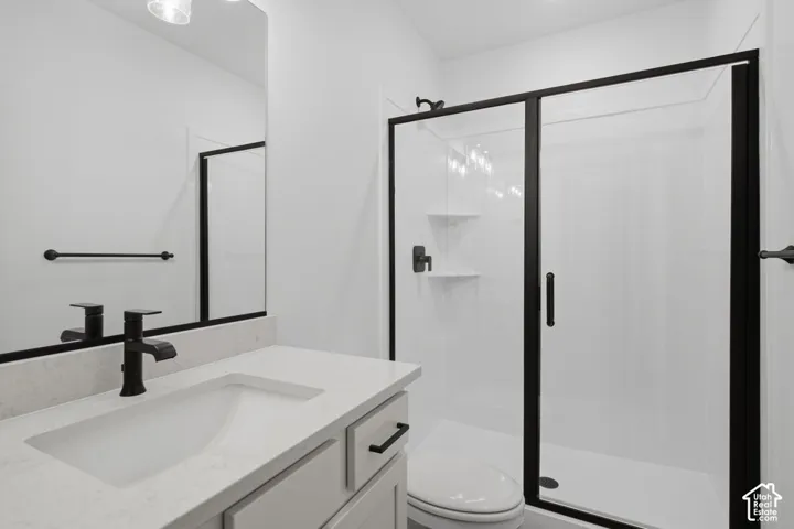 Vanity featuring a light-toned countertop with an integrated sink, matte black hardware, a shower enclosure with a glass door and matte black frame, and a frameless mirror