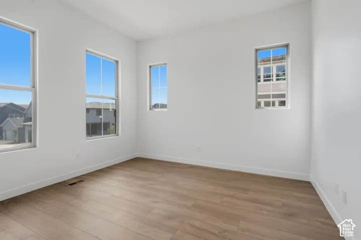 Neutral interior room featuring wood-finish flooring, crisp white walls, and four vertical windows