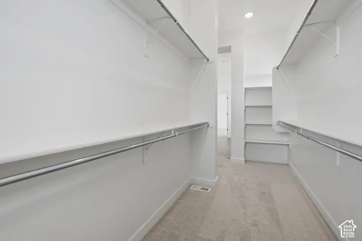 Walk-in closet featuring dual-level metal hanging rods, tiered built-in shelving, carpet flooring, and recessed ceiling lighting