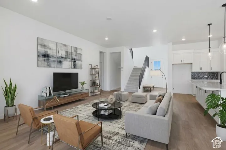 Open-concept living space featuring wood-finish flooring, recessed lighting, white cabinetry, a kitchen island with stone-finish countertops, and a staircase with a metal railing