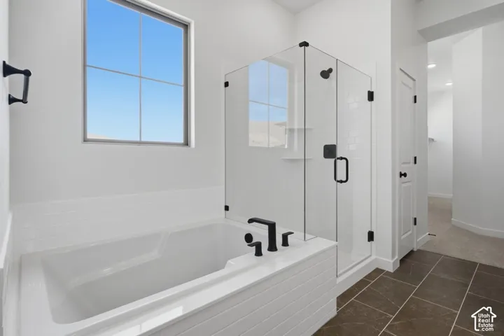 Deep soaking tub with a tiled surround, glass-enclosed shower, matte black plumbing fixtures, and dark-toned floor tiling