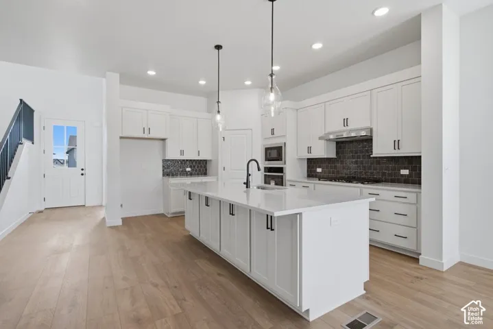 Kitchen featuring white cabinetry, quartz countertops, a central island with a matte black faucet, wood-finish flooring, and a tiled backsplash