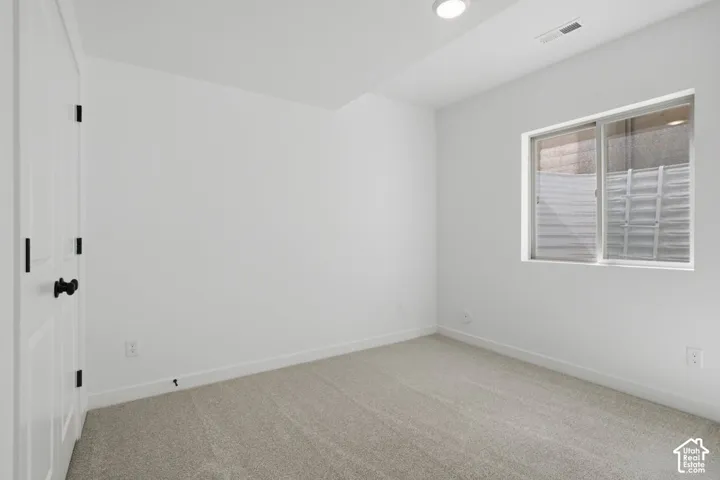 Neutral-toned carpeted flooring, white walls, recessed ceiling lighting, sliding window with a corrugated metal window well, and a closet with white paneled doors and matte black hardware