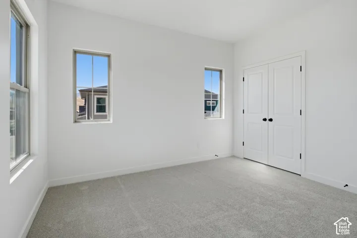 Bright room featuring neutral-toned carpeting, white walls, three single-pane windows, and a set of double-panel doors with matte black hardware