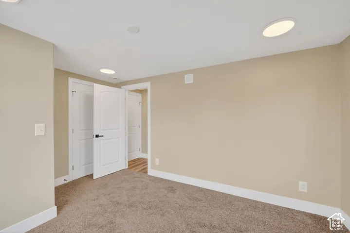 Neutral wall-toned room featuring recessed lighting, plush carpeting, white multi-panel interior doors with matte black hardware, and wood-finish flooring visible through the doorway