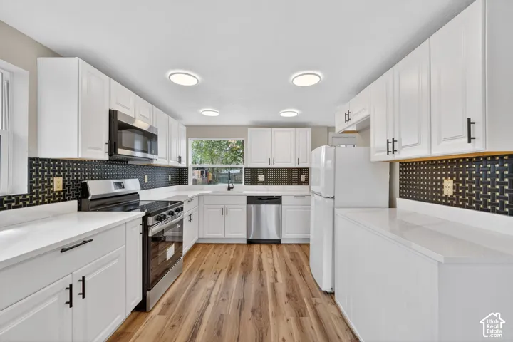 Kitchen featuring white shaker-style cabinetry, quartz countertops, geometric pattern backsplash, stainless steel appliances, and wood-finish flooring