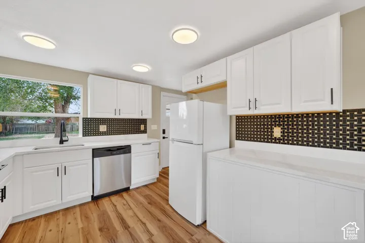 Kitchen featuring white shaker-style cabinetry, a contrasting basket-weave pattern tile backsplash, wood-finish flooring, and a stainless steel dishwasher