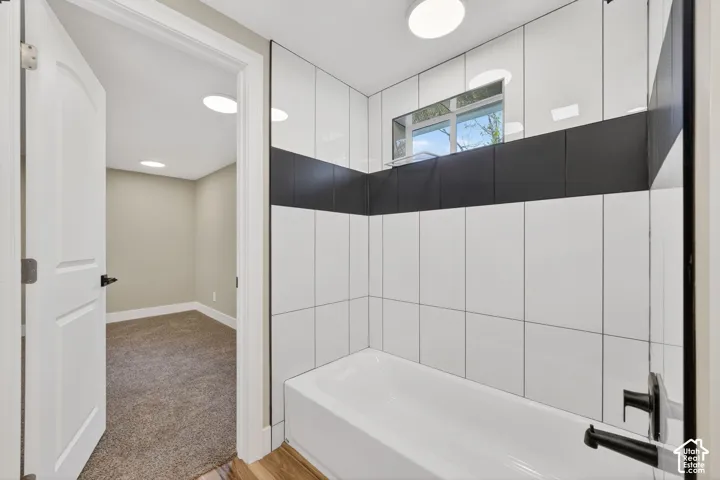 Bathtub enclosure featuring floor-to-ceiling white rectangular wall tiles with a horizontal dark tile accent stripe, integrated transom window, and matte black plumbing fixtures