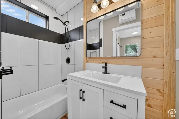 Bathroom featuring wood-plank walls, a white vanity with a rectangular sink, matte black hardware, and a tub-shower combination accented by large-format white and black tiling