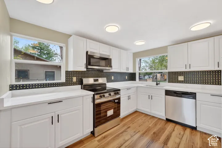 Kitchen featuring white cabinetry, solid-surface countertops, geometric tile backsplash, stainless steel appliances, and wood-finish flooring