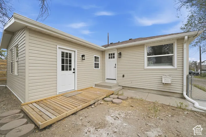 Exterior featuring beige horizontal siding, two white paneled doors with glass inserts, wood-finish decking, and matte black wall-mounted fixtures
