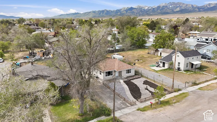 Single-story residence featuring a shingled roof, neutral-tone exterior siding, landscaped front yard with decorative stone and mulch, wood-post fencing, and a mountain backdrop